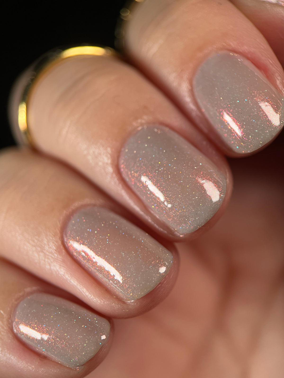A close-up of a hand with soft grey painted nails against a black background.