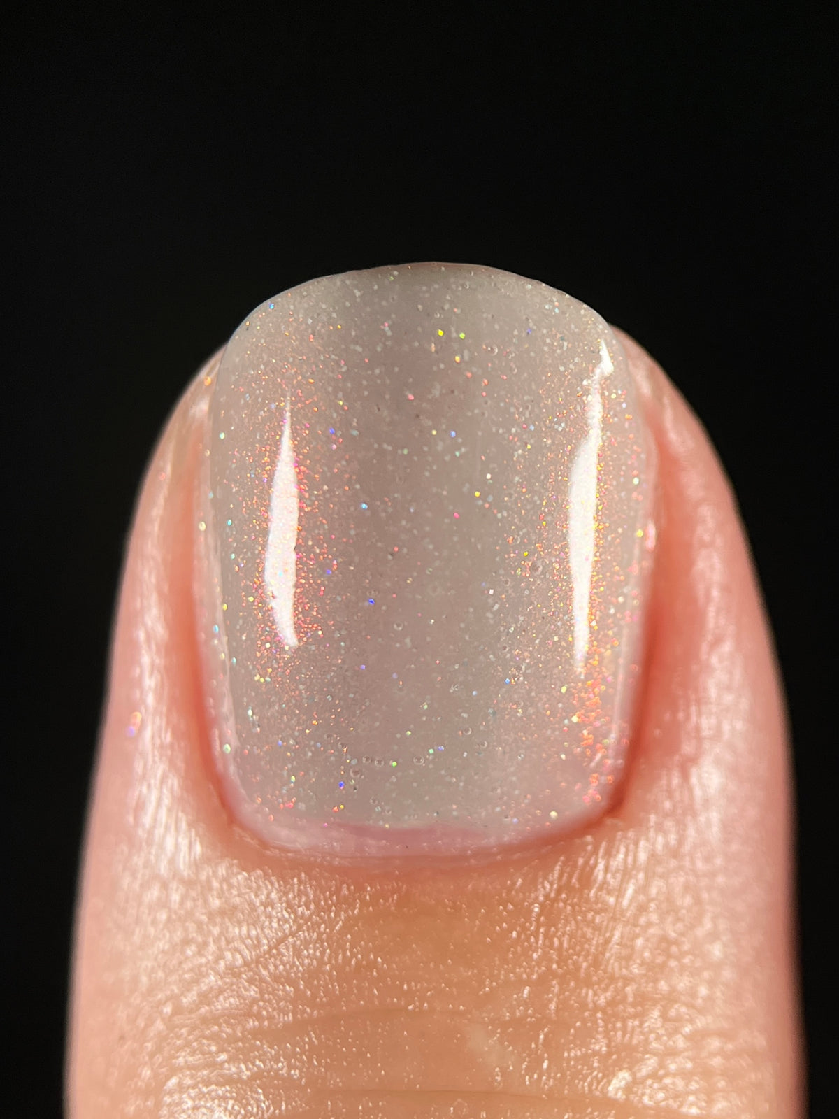 A close-up of a fingernail painted with a grey nail polish showing fine glitter and subtle pink-gold shimmer against a black background.