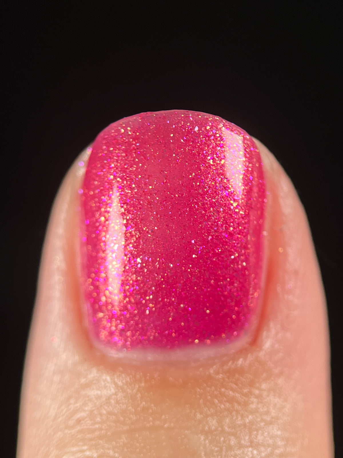 A close-up of a fingernail painted with a glittery pink nail polish against a solid black background.