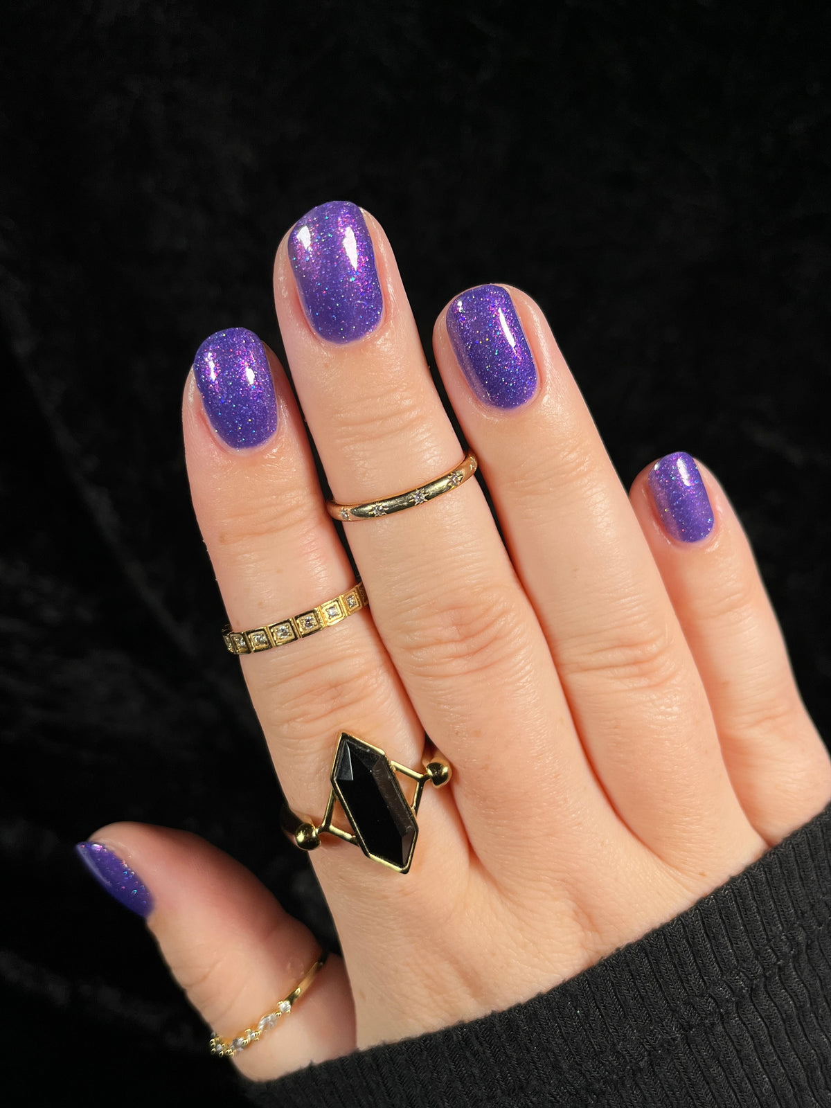 A close-up of a hand with glittery purple nail polish set against a dark textured background.
