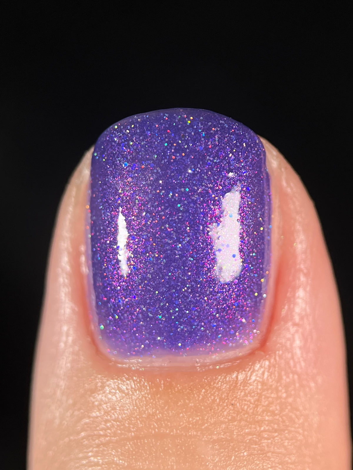 A close-up of a fingernail painted with a sparkling purple nail polish set against a solid black background.
