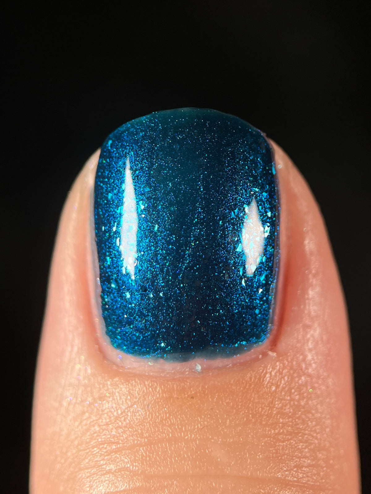 A close-up of a fingernail painted with a glittery metallic blue nail polish against a solid black background.