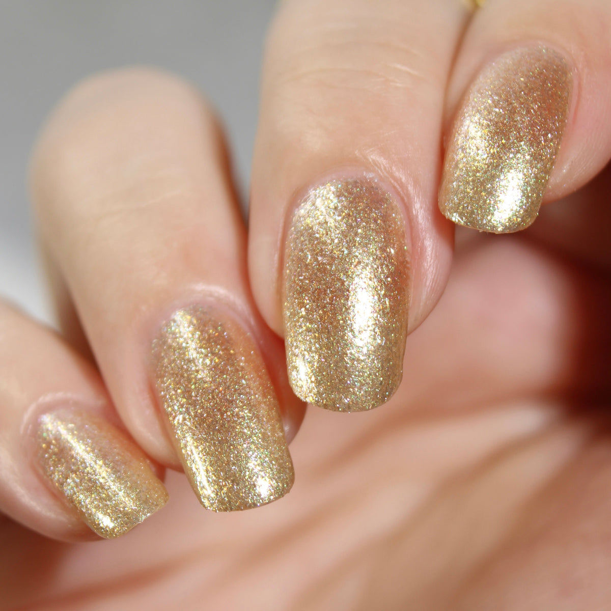 A manicured hand wearing a champagne gold nail polish.