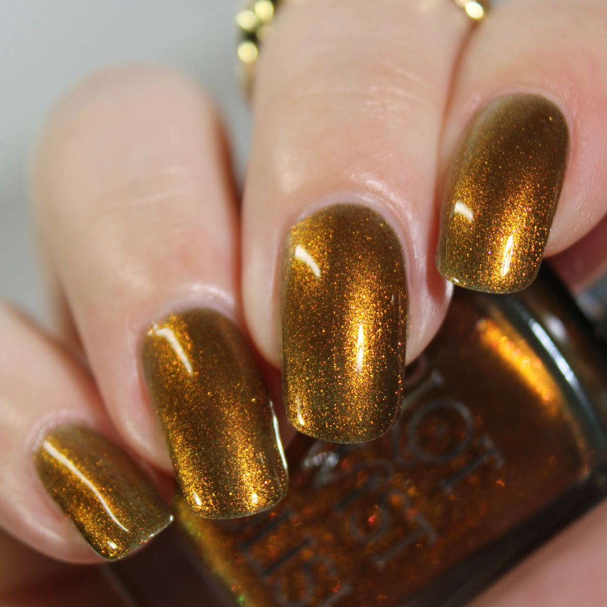 An up close manicure of a copper shimmer nail polish and a hand holding a bottle. 