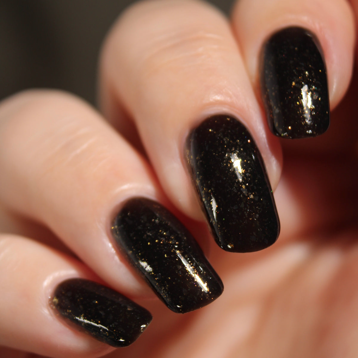 A manicured hand with a black polish with gold flakes. 