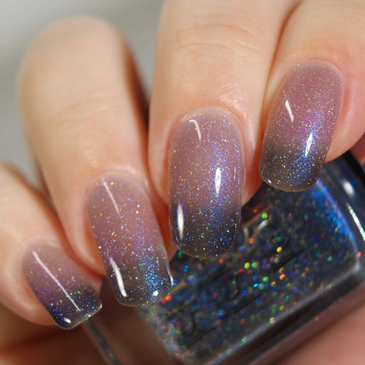 A manicured hand with a translucent shimmery nail polish base and blue nail tips holding a bottle of nail polish.