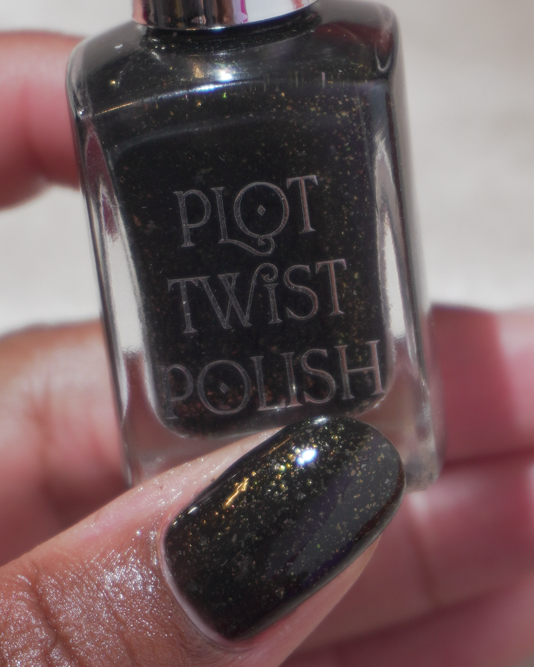 A close up photo of a thumb wearing a black polish and holding a nail polish bottle.