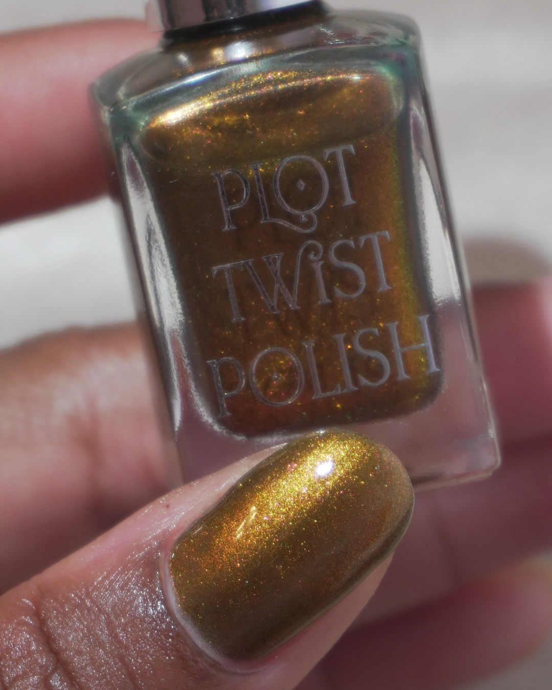A close up photo of a thumb wearing a copper polish and holding a nail polish bottle.