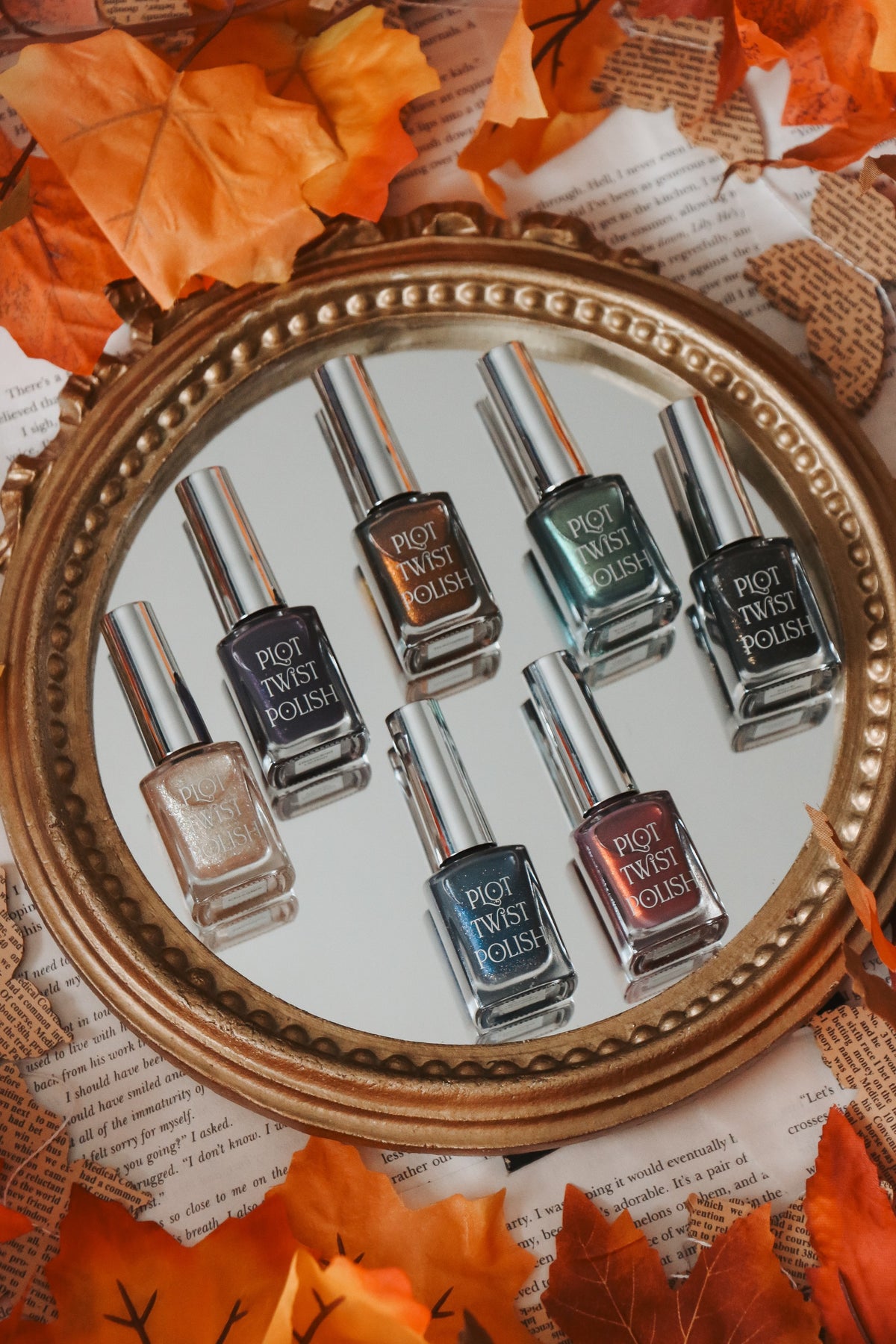 Six bottles of nail polish sitting on a mirror with leaves surrounding it. 