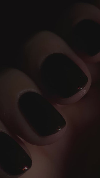 Close up video of a hand wearing dark brown nail polish with a light going over the polish at different angles. 