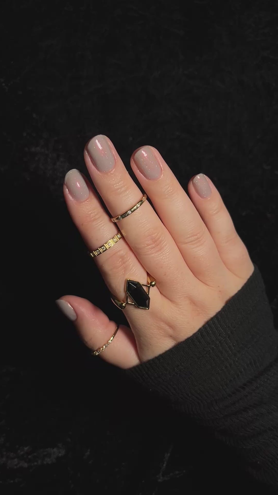 A close-up of a hand with soft grey painted nails against a black background.